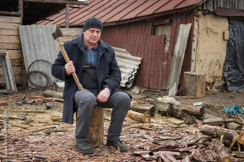 Slika na platnu Mature man with an axe sitting on a log