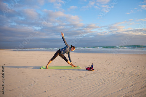 Woman on a yoga-mat the beach doing yoga pose