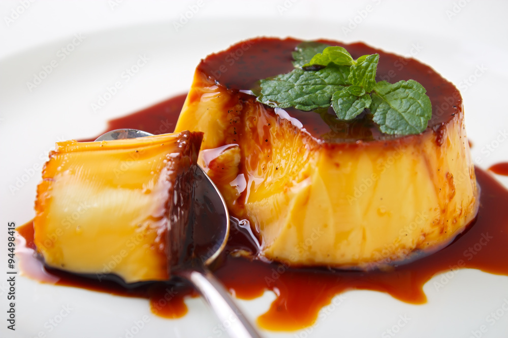 Caramel custard pudding and spoon on plate with lemon balm leave on top