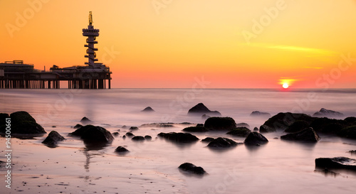 Sunset at Scheveningen, the Netherlands with a setting sun, rocks, the pier and silky smooth water