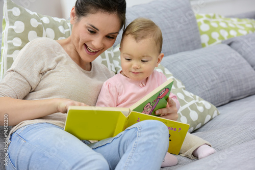 Mother and daughter reading book sitting in sofa