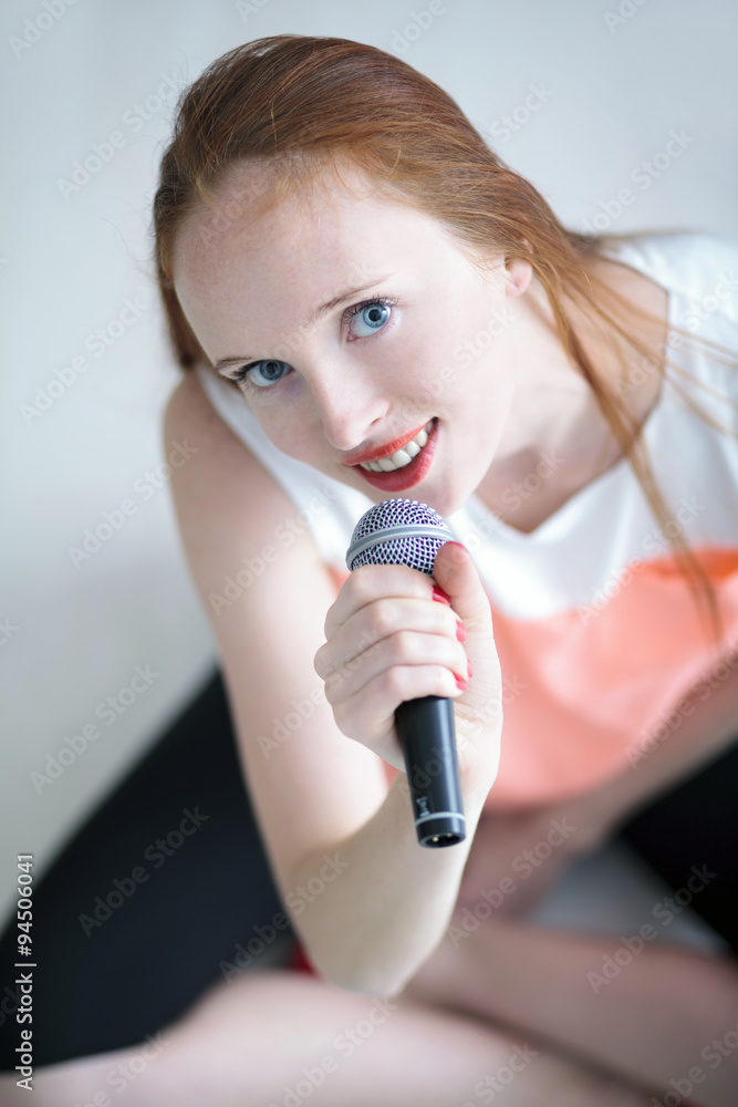 Attractive long haired young woman singing with a microphone and sitting on floor Attractive long haired young woman singing with a microphone and sitting on floor
