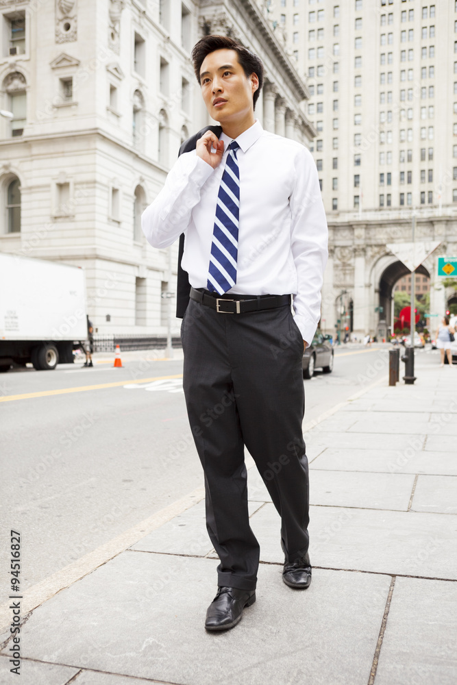 A young well dressed man with Jacket over shoulder walks down a city street. A young well dressed man with Jacket over shoulder walks down a city street.