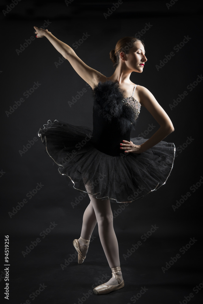 Beautiful ballerina in the role of a black swan, wearing black tutu and pointe shoes on black background
