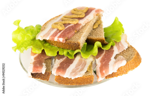 Sandwich with bacon slices, salad and mustard on rye bread on a