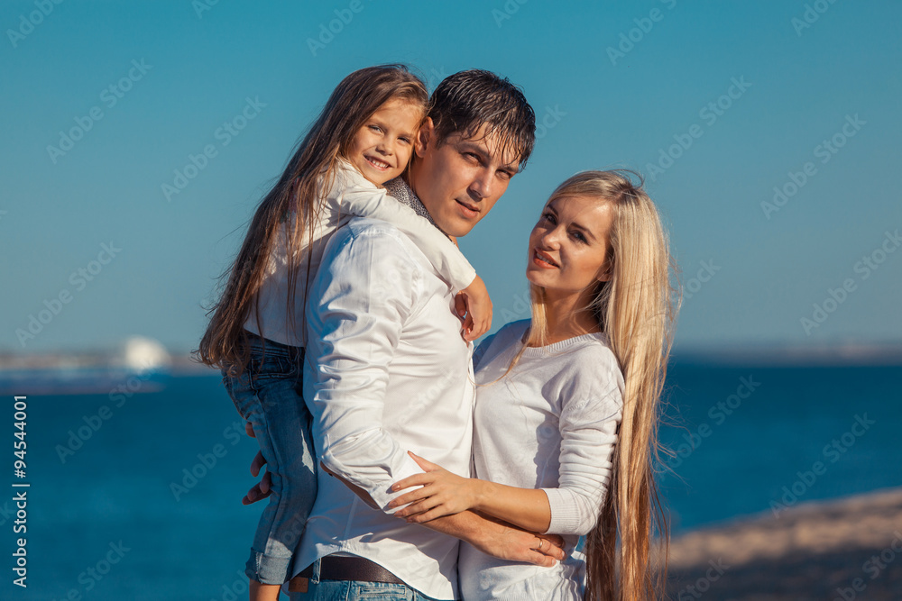 Young family in blue jeans hugging on the background of water