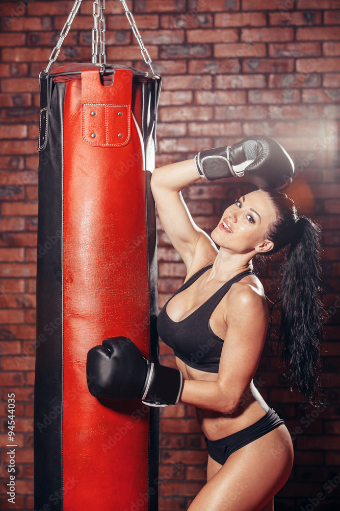 Young sexy girl with boxing gloves, punching bag, on the background wall of red brick