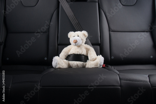 Teddy bear strapped in with seat belt in back seat of car