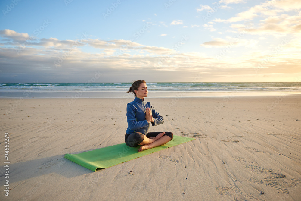 Young woman sitting cross-legged on the beach meditating