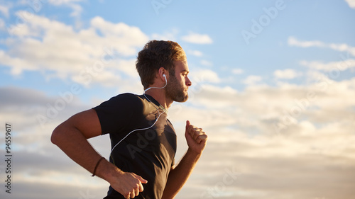 Obraz na plátne Man jogging on the beach with earphones