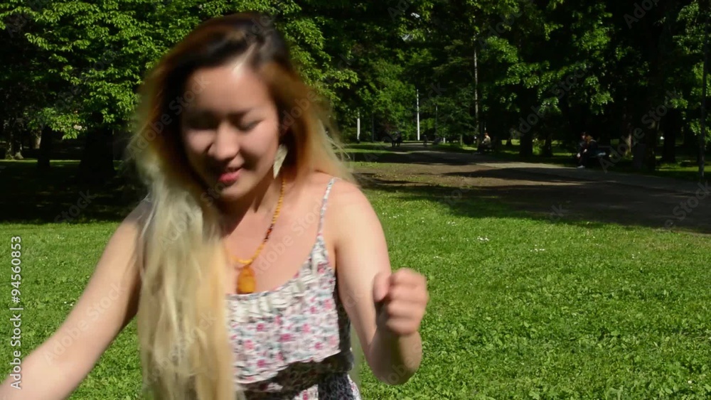 young attractive asian woman plays that she rides imaginary car in the park