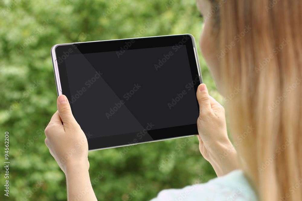 a woman holds a tablet in hands on background of leaves