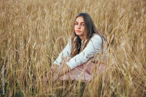 Young woman wearing dress sitting in field with wheat