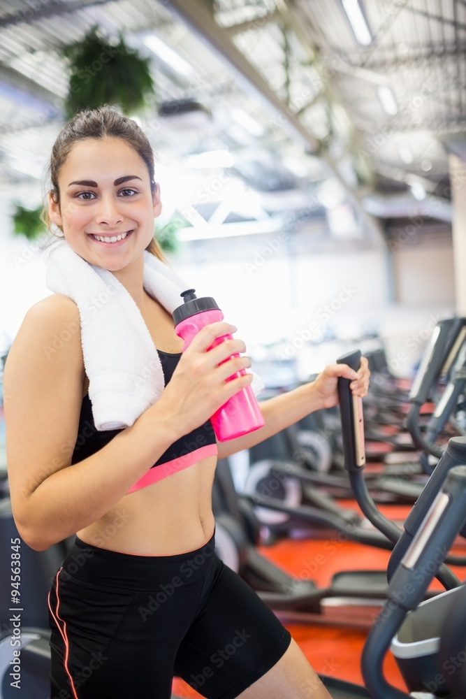 Fototapeta premium Smiling woman drinking on the cross trainer