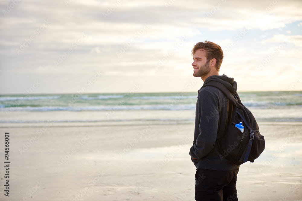 Man standing alone on a beach wearing a backpack Man standing alone on a beach wearing a backpack