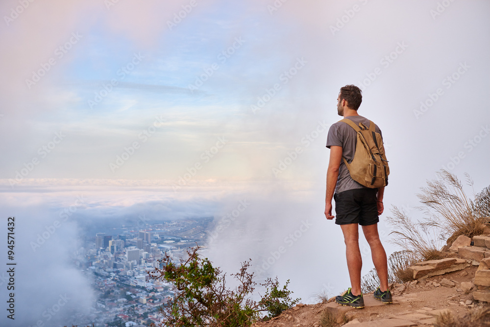 Hiker looking at the city through clouds on a mountain trail