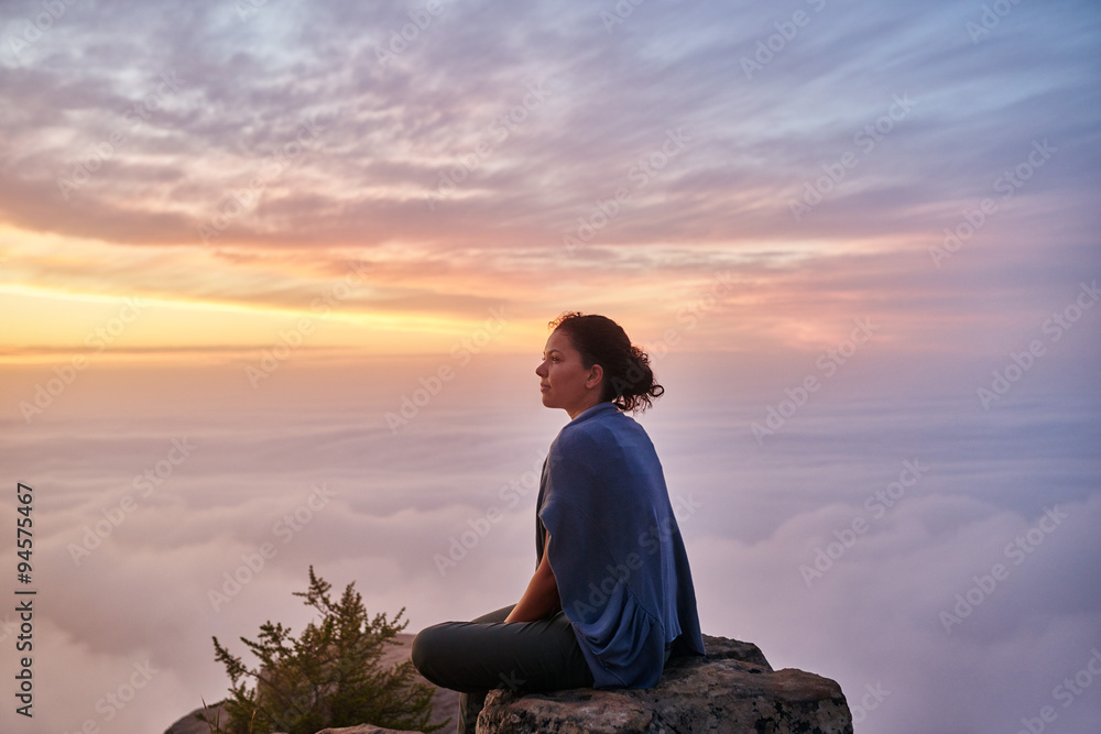 Woman sitting serenely on a mountain top in early morning
