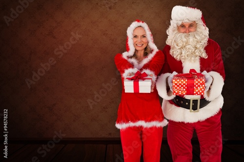 Composite image of santa and mrs claus holding gifts