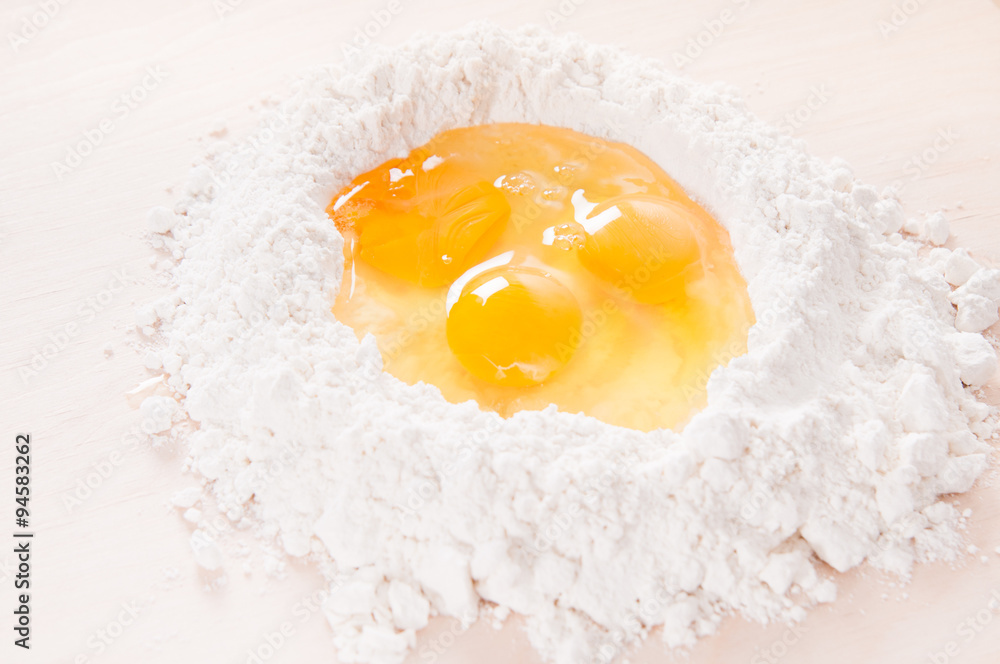 Three raw eggs in flour well on wood (making egg pasta dough) Three raw eggs in flour well on wood (making egg pasta dough)