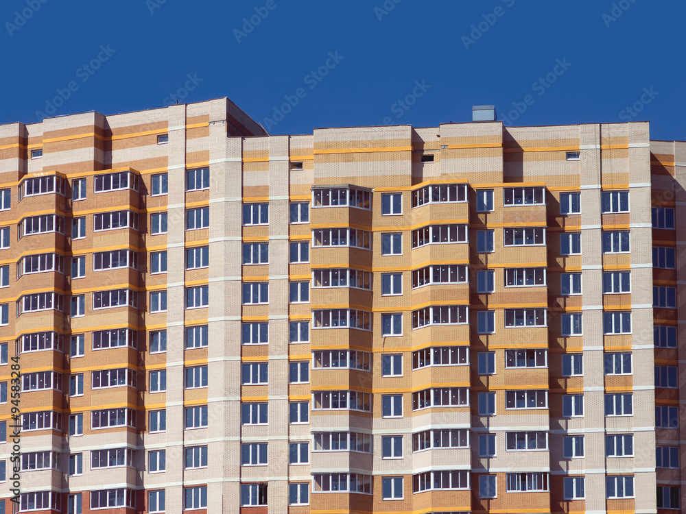Fototapeta premium Top section of multi-storey modern building constructed from bricks over clear blue sky