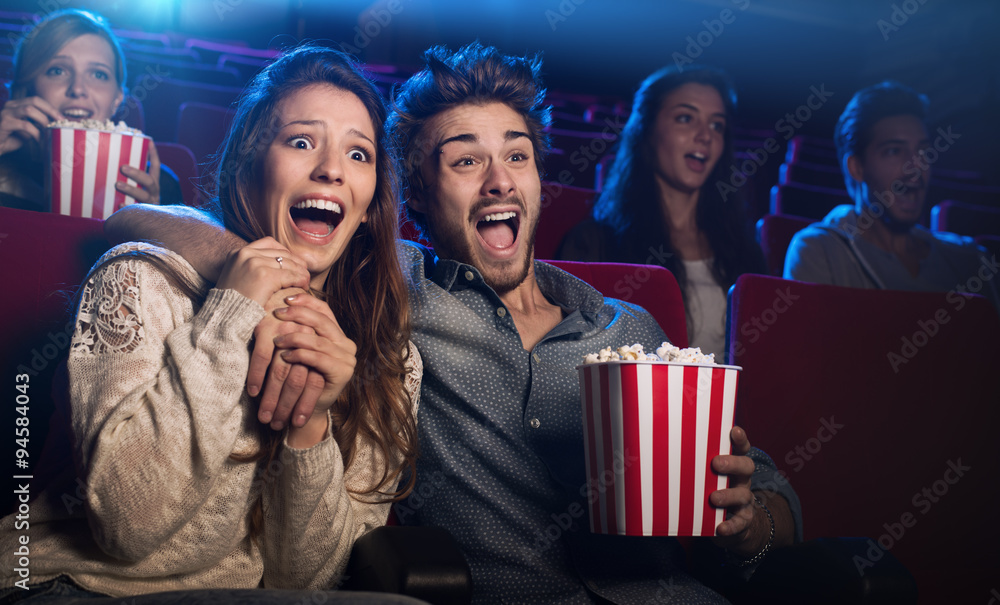 Young couple at the cinema watching an horror movie - obrazy, fototapety, plakaty 
