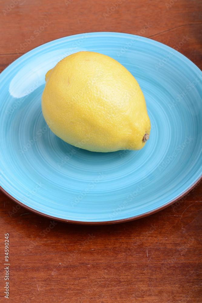 Whole lemon on a blue plate on wooden background