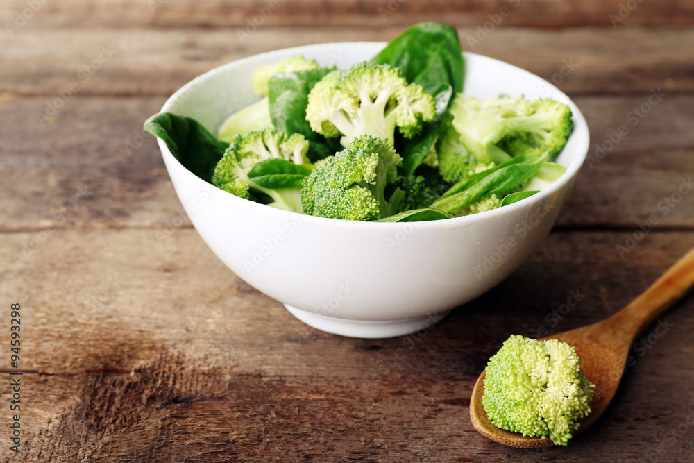 Fresh broccoli with spinach in bowl on wooden table close up Fresh broccoli with spinach in bowl on wooden table close up