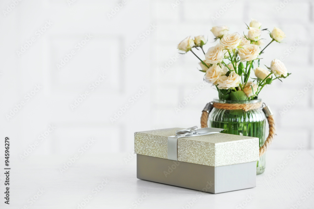 Fototapeta premium Big beautiful gift box with bouquet of flowers on the table in front of brick wall, close up