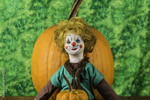 antique porcelain clown doll holding orange pumpkin on green background