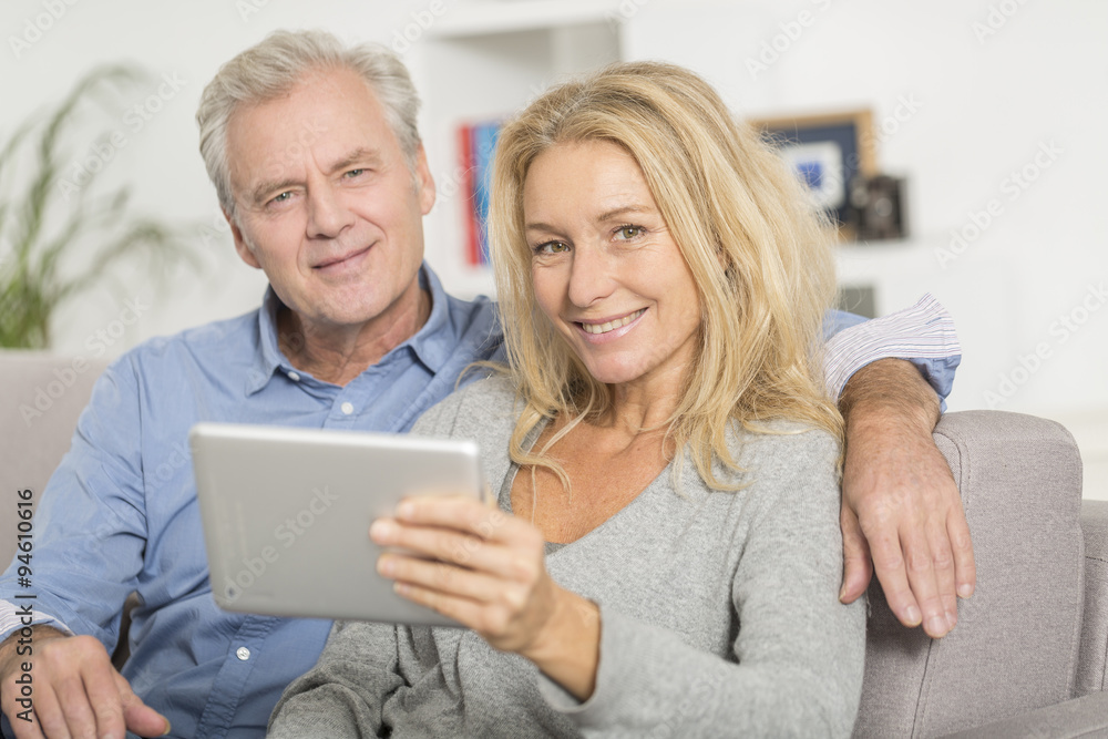 Mature couple sitting in sofa and using tablet pc Mature couple sitting in sofa and using tablet pc