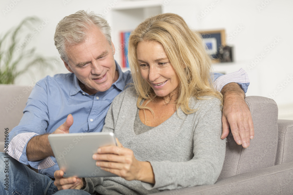 Mature couple sitting in sofa and using tablet pc Mature couple sitting in sofa and using tablet pc