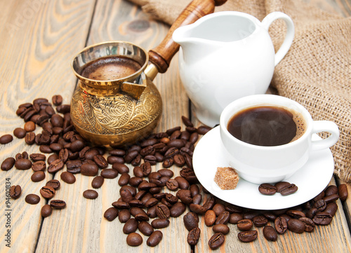 coffee cup with coffee beans, milk jug and turk on a wooden background