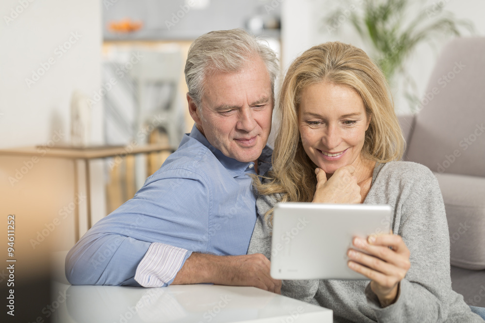 Mature couple sitting in sofa and using tablet pc Mature couple sitting in sofa and using tablet pc