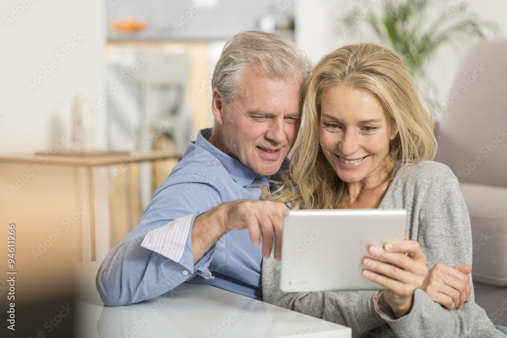 Mature couple sitting in sofa and using tablet pc Mature couple sitting in sofa and using tablet pc