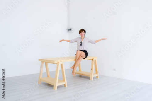 Smart Asian woman sitting on big pine table in white room.