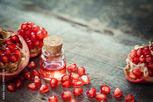 Pomegranate oil in bottle and garnet fruit with seeds on table.