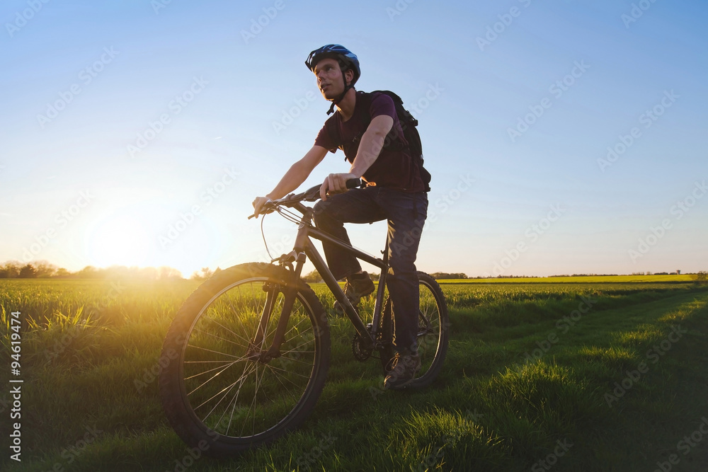 young sportive man riding bicycle outdoors at sunset