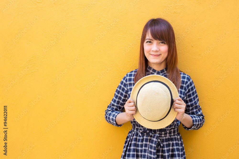 smiling woman wear in dress hand holding hat on yellow cement wall background smiling woman wear in dress hand holding hat on yellow cement wall background