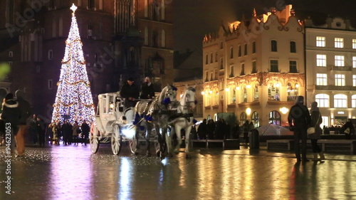 Traditionsl carriages of horses in festive harness passing Christmas tree at City Hall square decorated for holidays.