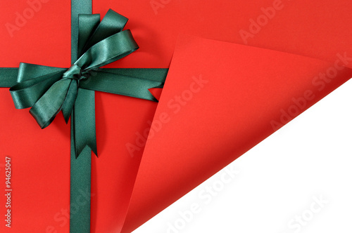 Green bow ribbon on red gift wrapping paper background folded open corner opening unwrapping birthday or christmas present photo