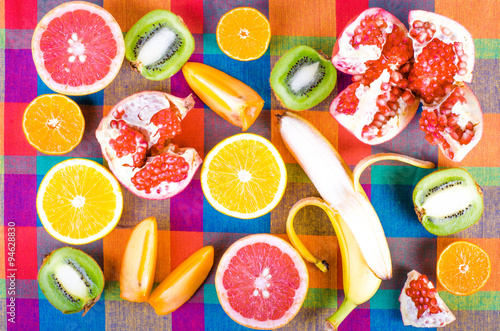 Fresh fruits on a colorful checkered kitchen towel. Raw and vegetarian eating background. Sliced orange, persimmon, kiwi, tangerine, banana, lemon, apple,  grapefruit, pomegranate, lime,  Top view