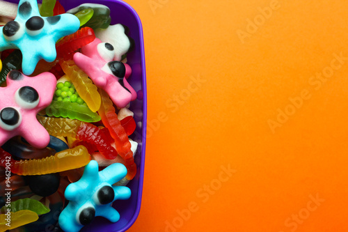 colorful jelly candies in the shape of a worm and a spider in a pot on orange background