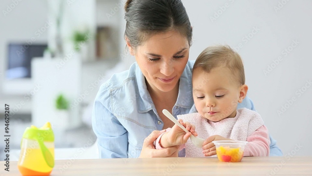 Young mother helping baby girl with eating by herself Young mother helping baby girl with eating by herself