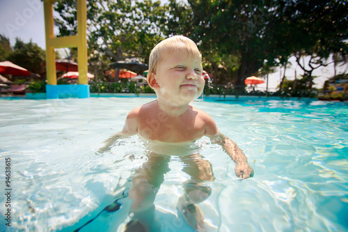 small blonde girl swims with joy in water of pool photo