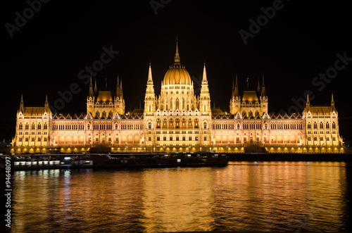 Night view of the famous Parliament building of Hungary in Budapest, illuminated by electric light. The reflections of electric lighting in the waters of the Danube River. 