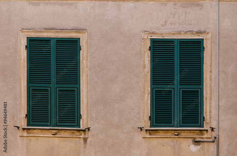 two old windows with wooden shutters on a weathered stone  exterior building wall