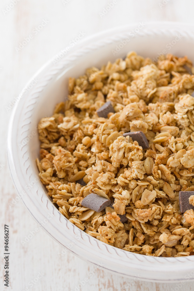 granola with chocolate on white bowl on white wooden background granola with chocolate on white bowl on white wooden background