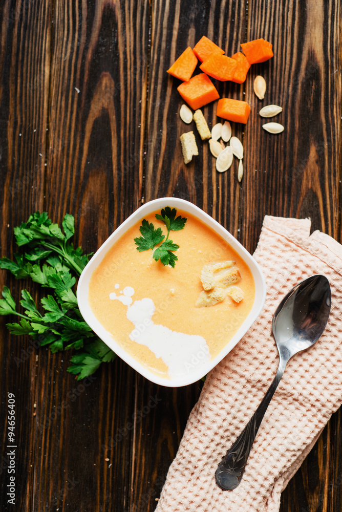 mashed pumpkin soup in a clay plate with herbs , cream , crackers and bread with sesame seeds on a wooden background mashed pumpkin soup in a clay plate with herbs , cream , crackers and bread with sesame seeds on a wooden background