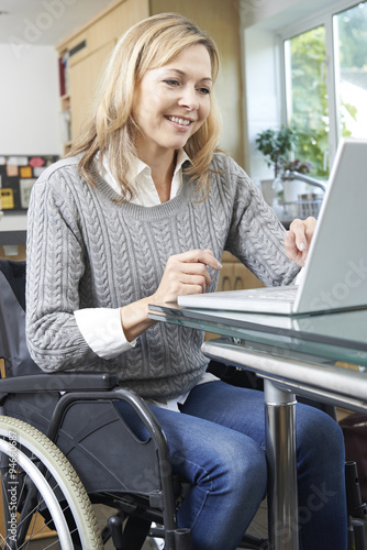 Disabled Woman In Wheelchair Using Laptop At Home