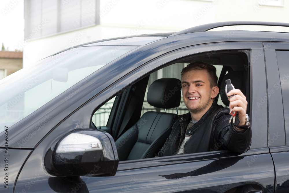 Young man smiling in drivers seat of new car showing keys
